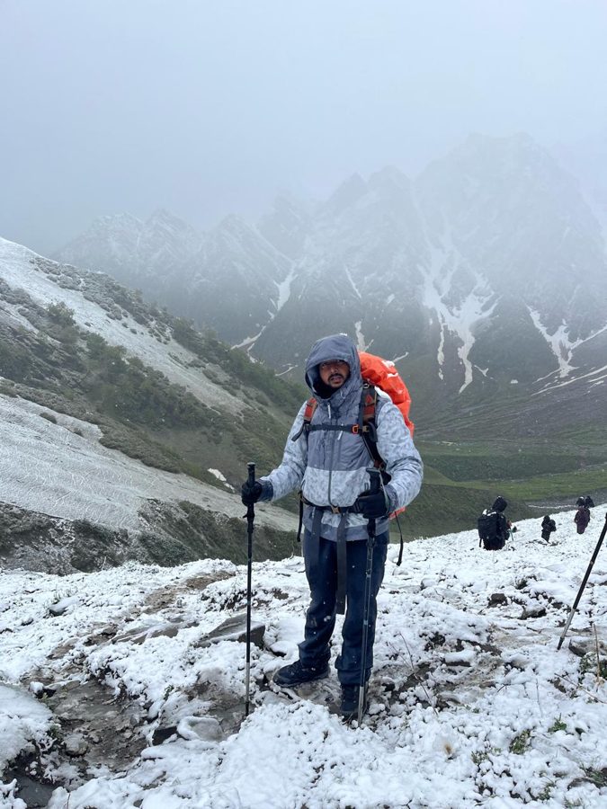 Tanmay trekking in snow with poles and an orange rucksack cover